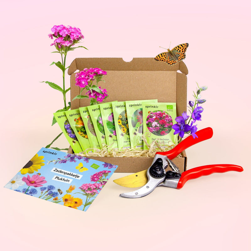 Doosje met daarin groene biologische zadenzakjes van Sprinklr, een rode snoeischaar, met bloemen en een vlinder om het doosje