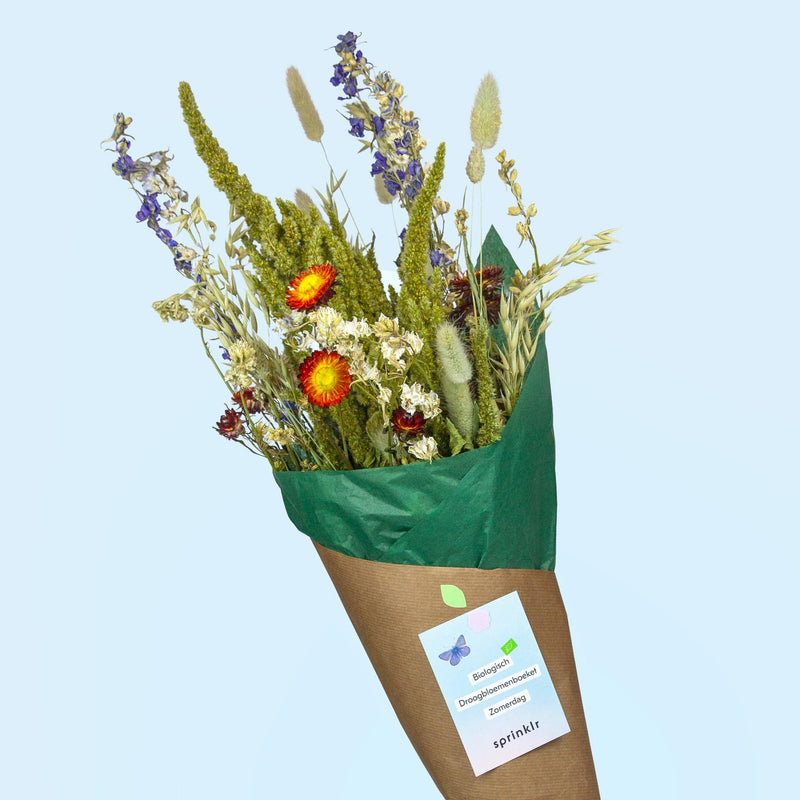 Boeket van biologische droogbloemen met verschillende tinten rood, geel en blauw in een groen papiertje